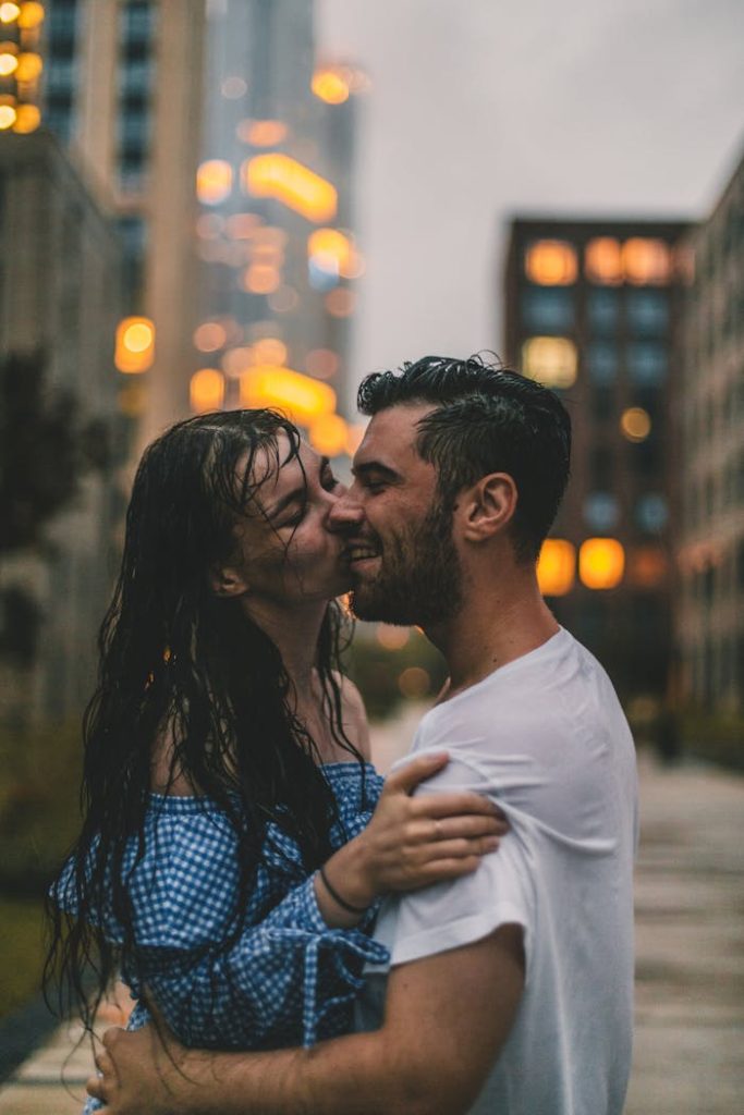 A couple embraces in the rain, surrounded by city lights, exuding warmth and togetherness.