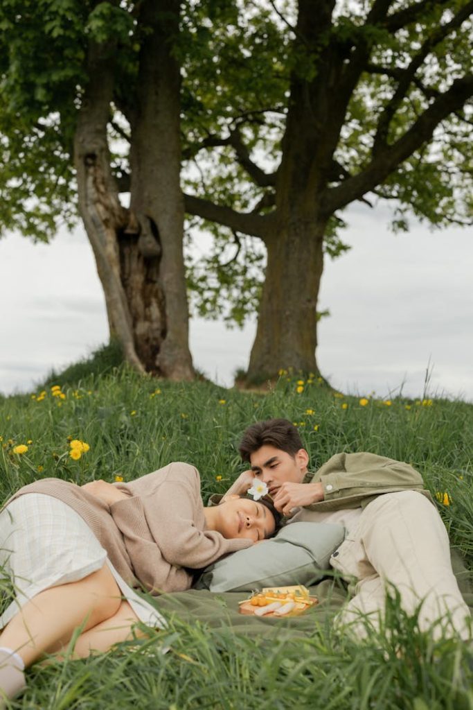A young couple enjoying a peaceful picnic outdoors in a meadow surrounded by trees.